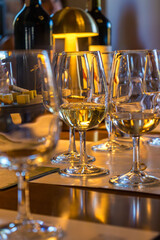 Close-up of glasses of white wine during tasting. The drink is poured from the bottle into a transparent glass, a warm golden atmosphere is created around. A stylish and atmospheric shot, perfect for