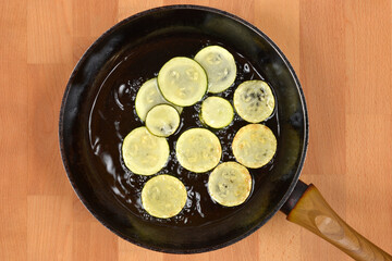 Zucchini slices frying in a pan with hot oil on a wooden surface