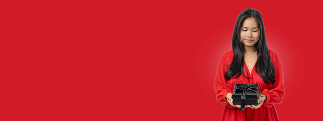 A woman in a red dress admires a black gift box