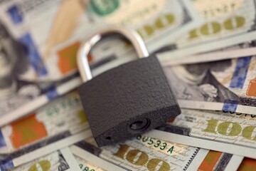 Small black padlock lies on big amount of new hundred US dollar bills