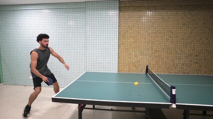 Male athlete playing table tennis, striking ball with precision near sleek tiled wall, capturing intense competitive moment during indoor match - Powered by Adobe
