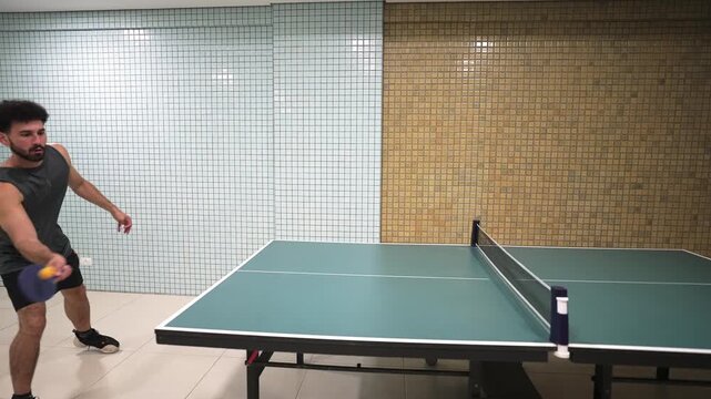 A young man makes a dynamic forehand play in a game of table tennis. This energetic shot is perfect for content about sports, recreation, and active lifestyles.