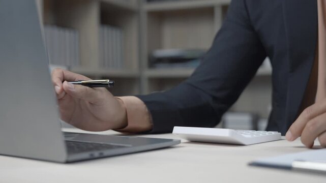 Financial professional meticulously calculating corporate data using laptop and calculator, intently analyzing business metrics and investment strategies while working at office desk