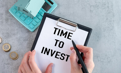 A person is writing the word Time to Invest on a piece of paper.
