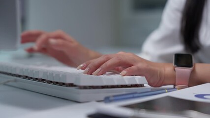 Female professional wearing pink smartwatch typing efficiently on white keyboard, capturing focused data entry moment within sleek corporate office workspace - Powered by Adobe