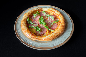 Delicious Pizza Delight: A tantalizing close-up shot of a freshly baked pizza, garnished with savory ingredients, rests on a ceramic plate, all against a dark background.