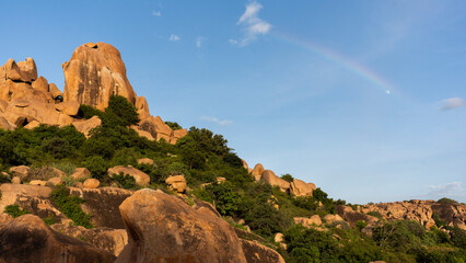 A view of Hampi's golden boulders with a rainbow and the moon at sunset.