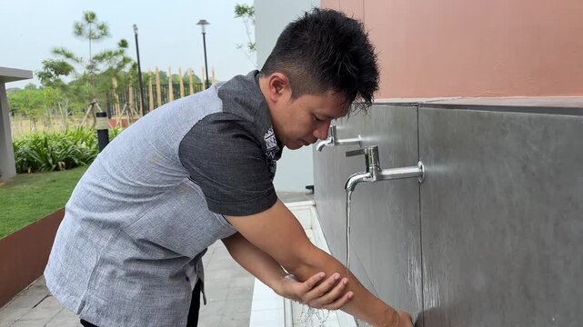 Muslim man washing arm with clean water from faucet during ablution ritual before Islamic prayer outdoors