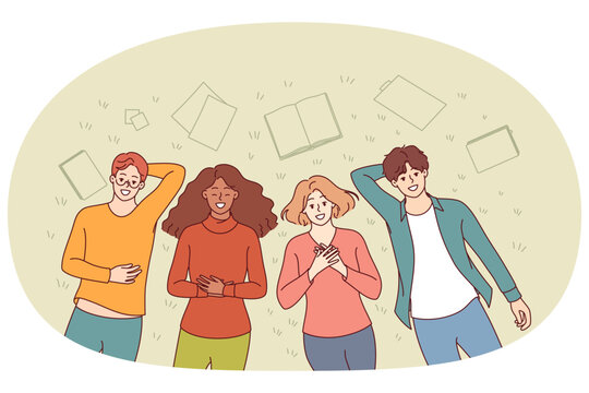 Group of happy students lie on grass in park and smile, enjoying sunny summer day. Positive guys and girls are relaxing in park, throwing textbooks aside and forgetting about studies.