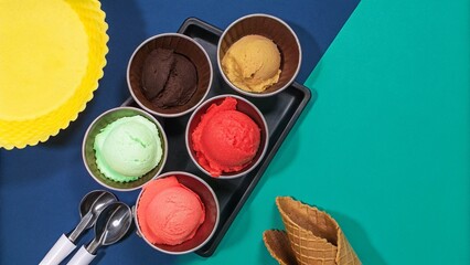 Assorted scoops of ice cream on blue background, top view, copy space. Various ice creams or gelato with waffle cones, healthy summer dessert creative concept.