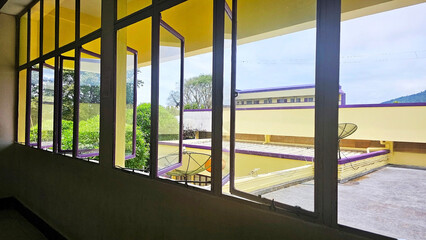 View from the Window: A spacious room with yellow wall colors and window frames, providing an appealing view of outside with lush green landscape and the blue sky.