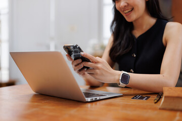 Smiling businesswoman using smartphone and laptop at office desk