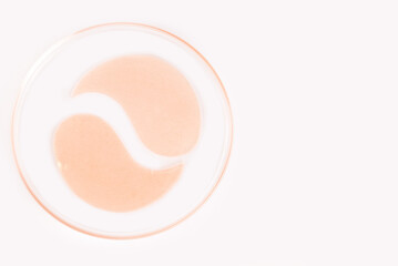 Cosmetic hydrogel eye patches in laboratory dish, light backdrop, authentic skincare product.