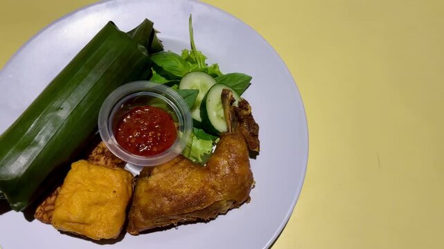 Indonesian food, fried chicken, tofu, tempeh, chili sauce and liwet rice is served on the table with camera movement from right to left