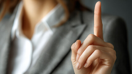 Pointing finger gesture, close-up view of hand dressed in professional attire against a neutral background expressing communication and authority in a corporate setting.