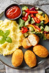 Delicious crispy fried breaded chicken croquettes served with potatoes, fresh salad and tomato sauce close-up in a plate on the table. Vertical top view from above