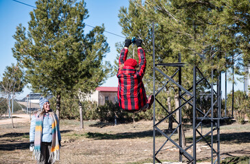 Middle-aged woman zip-lining outdoors while her friend watches and smiles during a fun winter getaway in the countryside