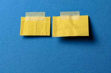 Pieces of blank yellow paper memo reminder notes with adhesive tape and copy space for text on blue background