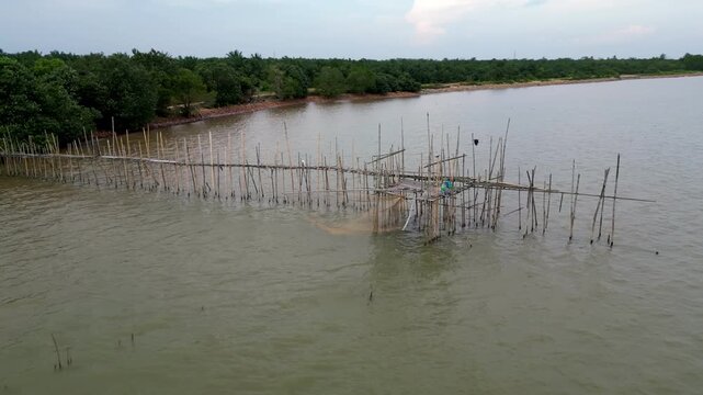 A body of water with a wooden fence on the shore. The water is murky and the fence is made of wood. Aerial view Pantai Parit Hailam, Batu Pahat