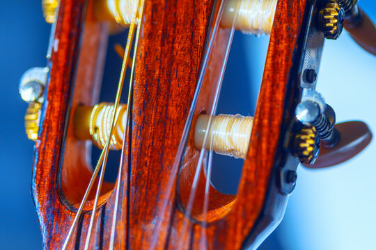 Details of a classical guitar headstock with nylon strings. Light reflects off the polished wood and nylon strings, highlighting the tuning pegs