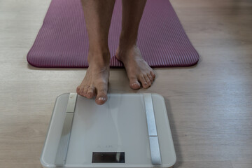 Man checking weight on digital scale for health monitoring.  Close-up of male feet on a modern digital scale placed next to a yoga mat at home. Concept of personal health tracking, body weight control