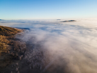 Clouds over the mountains and autumn forest at foggy sunrise. Aerial view. Autumn landscape