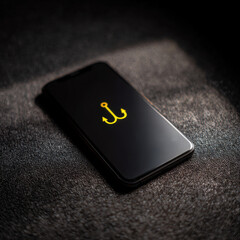 Smartphone lying on dark textured surface illuminating bright yellow anchor symbol in dim light with subtle shadows and reflections creating a moody atmosphere around it.