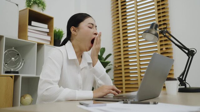 sleepy young woman yawning while working with laptop computer at home office