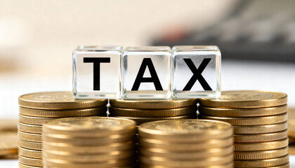 TAX text written on transparent glass cubes arranged on golden coins