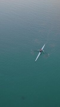Aerial view of a rower in a single scull boat, training on a calm lake. The rower is propelling the boat forward with oars, practicing for a competition.