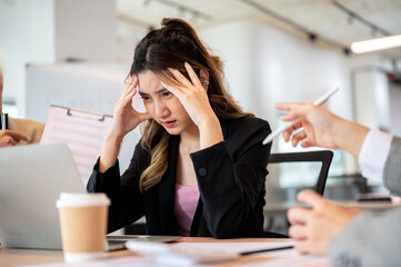 Asian businesswoman holding head getting stress or exhausted over workplace dispute at office table