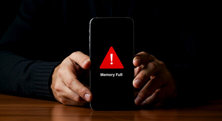 Person holding phone with memory full warning sign displayed on the dark screen of the device shown © Cerry