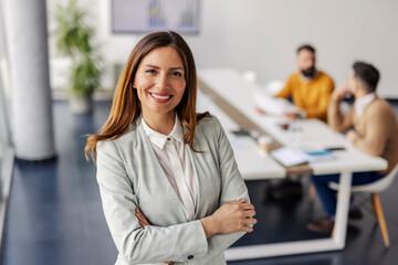 Confident Businesswoman in Light Gray Suit Smiling in a Professional Office with Colleagues in Background
