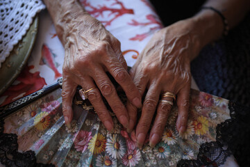 Le mani di una donna anziana sopra un ventaglio con ornamenti floreali