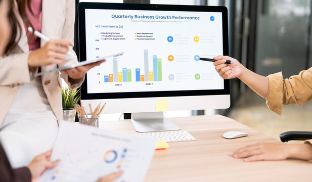 A close-up shot of a business team analyzing a digital dashboard displaying quarterly business growth and performance charts. They are using a stylus and a pen to point out key data.