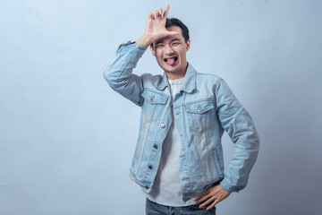 Fototapeta premium Asian man in denim jacket sticking out his tongue while making an 