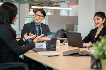 Smiling businessman and woman listening to coworker talking while sitting at wooden table in office.
