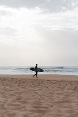 Surfer standing on the beach watching the ocean waves, lifestyle and adventure concept.