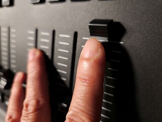 Close-up of a person's hand adjusting sliders on a lighting control console used in stage.
