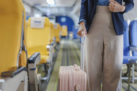 Businesswoman walking through airplane aisle pulling carry on luggage