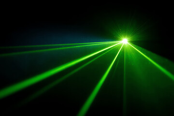 Bright green laser beams radiate from a single point in a dark environment, creating sharp, vivid light streaks that cut through the darkness with high intensity and clarity