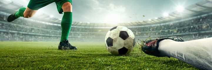 Banner. Player in green uniform kicking soccer ball while opponent in attempts sliding tackle on...