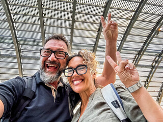 Middle-aged couple taking selfie at train station, smiling and happy before journey, enjoying travel, love, fun, adventure and togetherness, embracing youthful spirit, discovery and modern lifestyle
