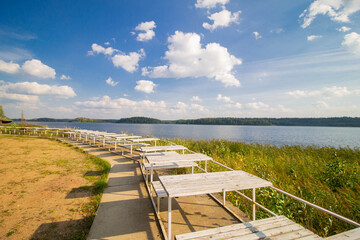 Row of Wooden Sunbeds Along Lakeshore Path Under Blue Sky &ndash; Serene Summer Resort Scene