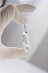 Vertical image. Closeup of human hand who wearing medical gloves and holding ampoule against bright background