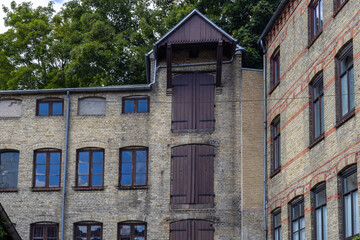 Tan Brick Building With Arched Windows And A Large Wooden Loading Bay Sits Next To A Similar Structure