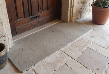 Obraz premium A detailed close-up of a rustic floor transition, showcasing the beautiful contrast between a rough concrete threshold and a smoother stone surface by a wooden door. 