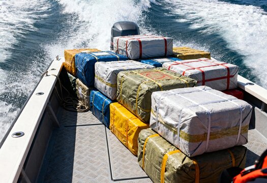 Speedboat transporting large wrapped packages across sea, concept of drug trafficking, narcotics smuggling, maritime security and law enforcement in international waters