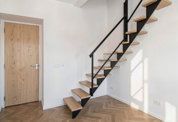 Fototapeta premium A modern industrial-style staircase featuring open wooden treads and a sleek black steel frame, creating a minimalist architectural focal point in a bright interior. 