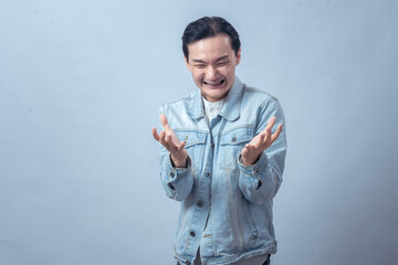 Asian man in denim jacket with shocked expression looking at his open palms, symbolizing surprise,...
